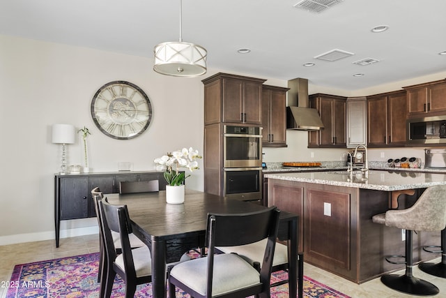 kitchen with stainless steel appliances, dark brown cabinets, light tile patterned floors, and light stone counters