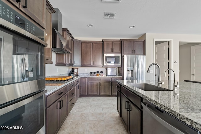 kitchen with wall chimney exhaust hood, stainless steel appliances, light stone countertops, and sink