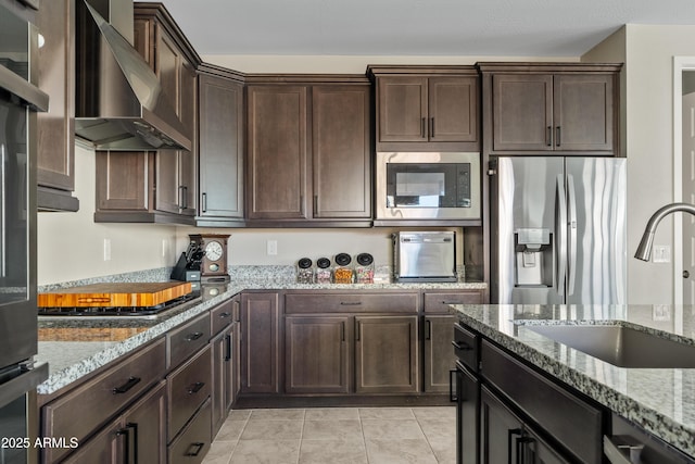 kitchen with wall chimney exhaust hood, appliances with stainless steel finishes, light stone countertops, and sink