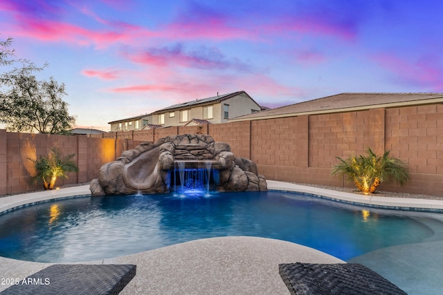 pool at dusk featuring pool water feature and a water slide