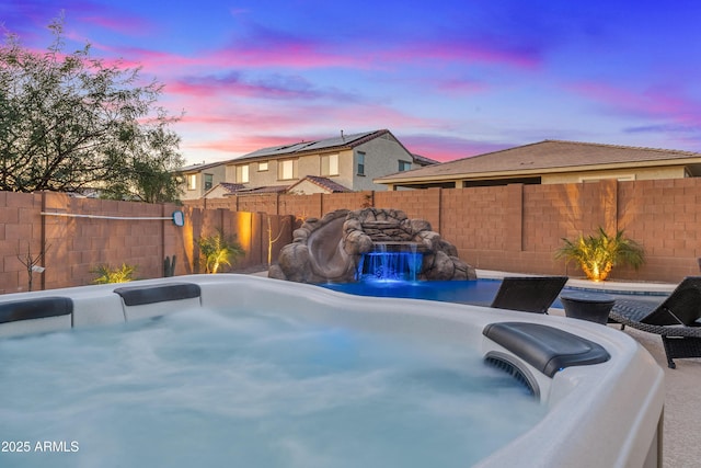 pool at dusk with a hot tub and pool water feature