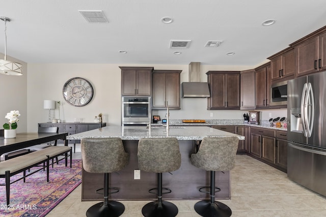 kitchen with appliances with stainless steel finishes, decorative light fixtures, light stone countertops, and an island with sink