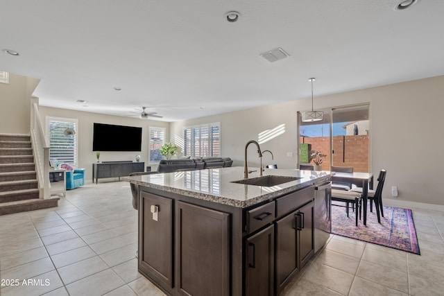 kitchen with sink, dark brown cabinetry, an island with sink, light tile patterned flooring, and stainless steel dishwasher