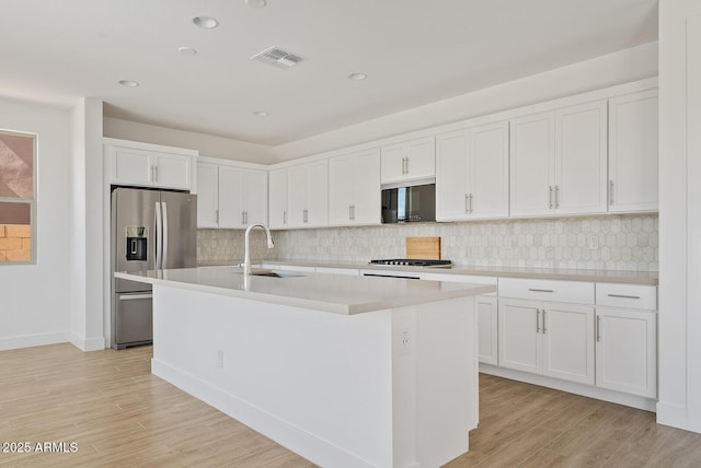 kitchen featuring stainless steel fridge with ice dispenser, white cabinetry, sink, light hardwood / wood-style flooring, and a center island with sink