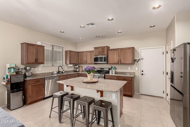 kitchen featuring light stone countertops, stainless steel appliances, a kitchen bar, a kitchen island, and visible vents