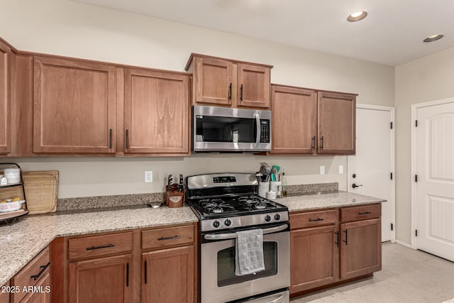 kitchen with brown cabinets, stainless steel appliances, and light stone countertops