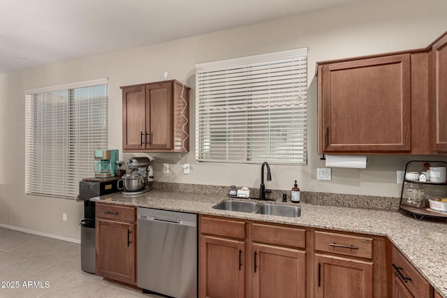kitchen featuring light stone counters, a sink, brown cabinetry, light tile patterned floors, and stainless steel dishwasher
