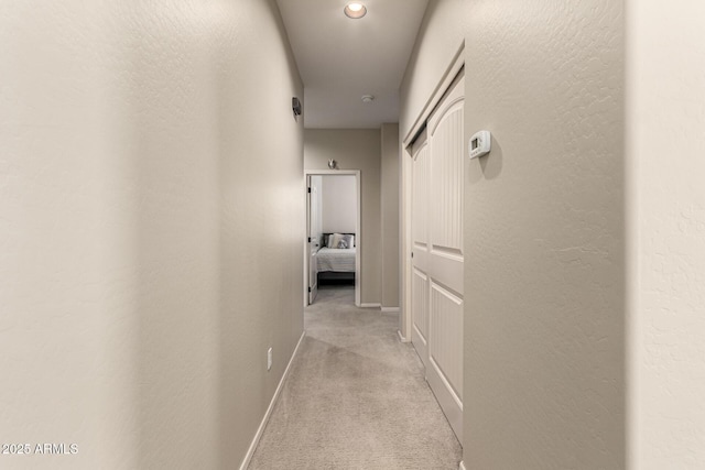 hall featuring a textured wall, baseboards, and light carpet