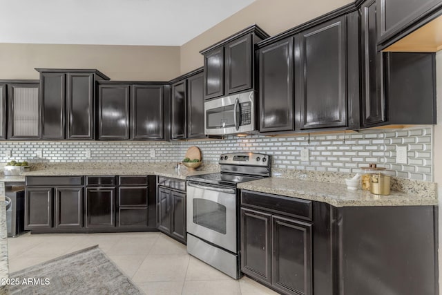 kitchen with light stone countertops, appliances with stainless steel finishes, backsplash, and light tile patterned floors