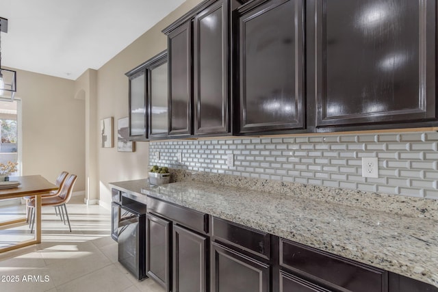 kitchen featuring dark brown cabinets, light tile patterned flooring, light stone countertops, and tasteful backsplash