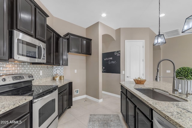 kitchen with light stone counters, stainless steel appliances, sink, pendant lighting, and light tile patterned floors