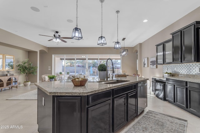 kitchen with dishwasher, a center island with sink, sink, hanging light fixtures, and light stone countertops