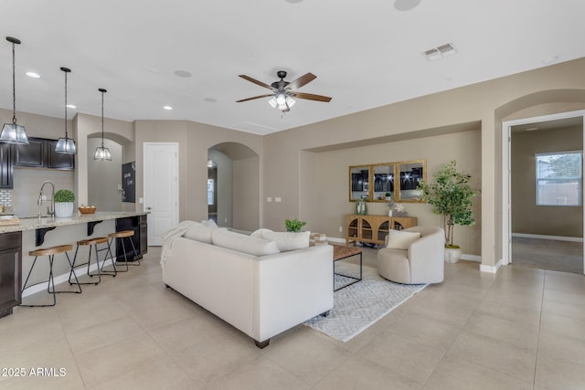 tiled living room with sink and ceiling fan with notable chandelier