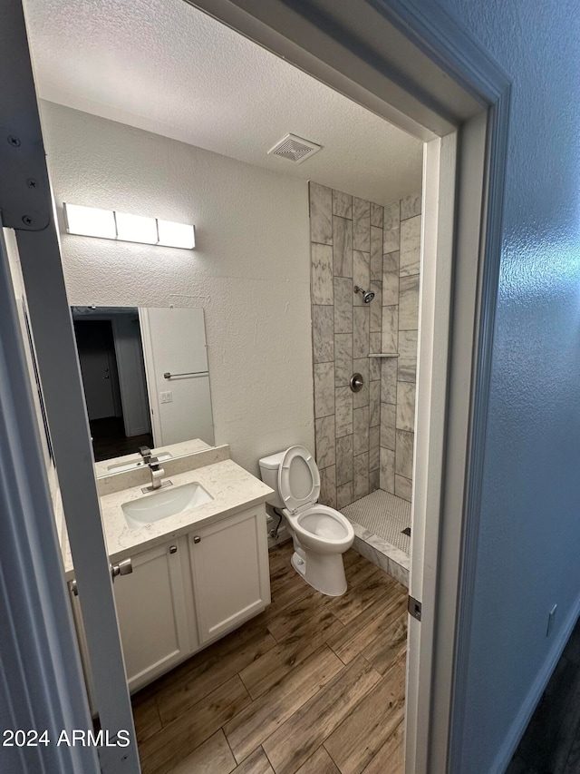 bathroom featuring a tile shower, a textured ceiling, vanity, and toilet