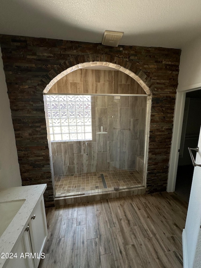 bathroom with hardwood / wood-style flooring, a textured ceiling, vanity, and tiled shower