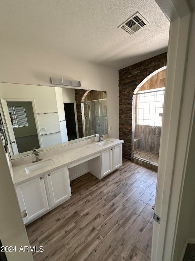 bathroom with hardwood / wood-style floors, walk in shower, vanity, and a textured ceiling