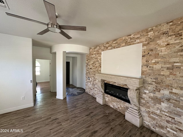 unfurnished living room featuring ceiling fan, a stone fireplace, a textured ceiling, and dark hardwood / wood-style flooring