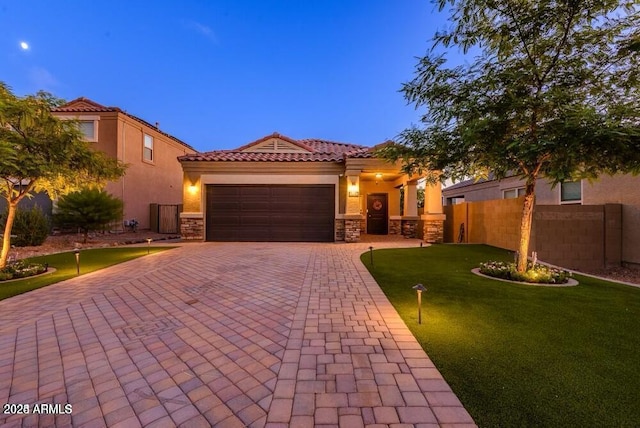 mediterranean / spanish house featuring decorative driveway, stucco siding, an attached garage, fence, and stone siding