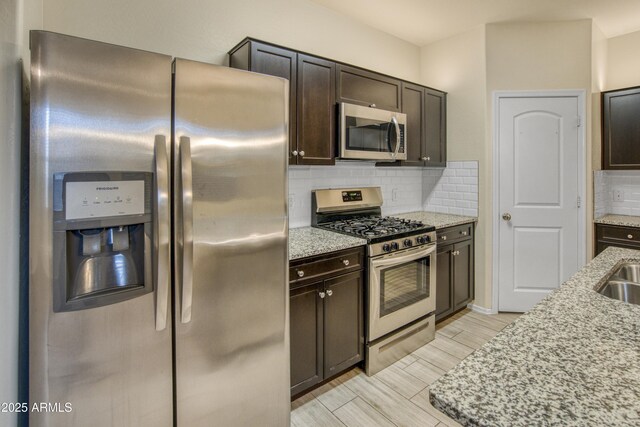 kitchen featuring appliances with stainless steel finishes, dark brown cabinetry, backsplash, and light stone countertops