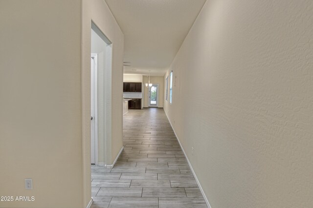 hall featuring a textured wall, baseboards, and wood finish floors