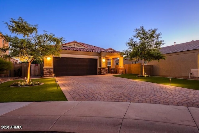 mediterranean / spanish-style home featuring an attached garage, a tiled roof, decorative driveway, and stone siding