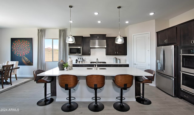 kitchen featuring stainless steel appliances, dark brown cabinets, a kitchen island with sink, pendant lighting, and exhaust hood