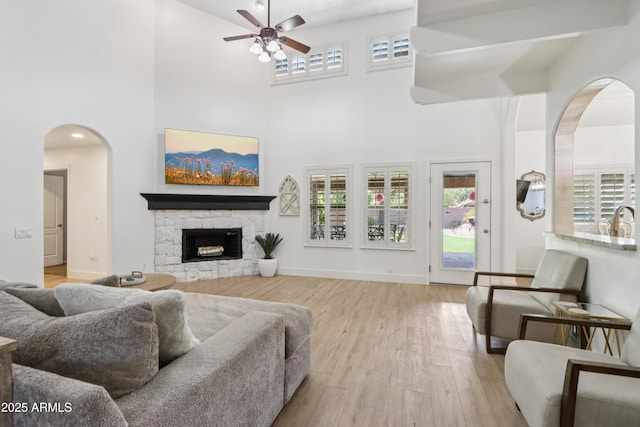 4735 E Harmony Cir, Mesa, AZ 85206 - living room featuring arched walkways, ceiling fan, wood finished floors, a towering ceiling, and a stone fireplace