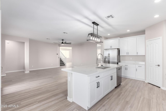 kitchen featuring an island with sink, appliances with stainless steel finishes, open floor plan, white cabinetry, and a sink