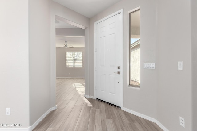 foyer entrance with light wood-type flooring, ceiling fan, and baseboards