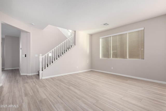 spare room featuring light wood finished floors, stairway, visible vents, and baseboards