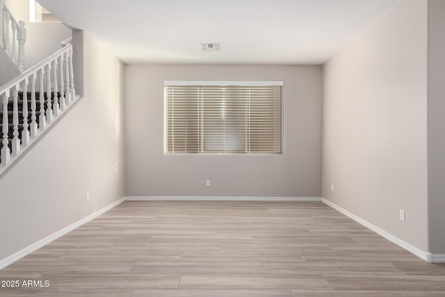 spare room with light wood-style floors, stairway, and baseboards