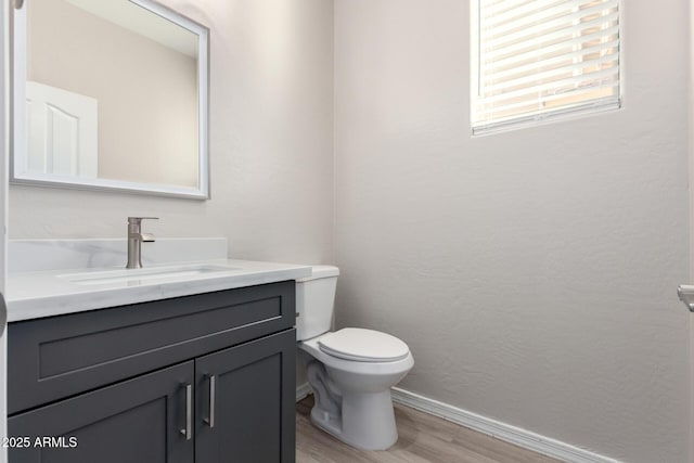 half bathroom featuring a textured wall, toilet, vanity, wood finished floors, and baseboards