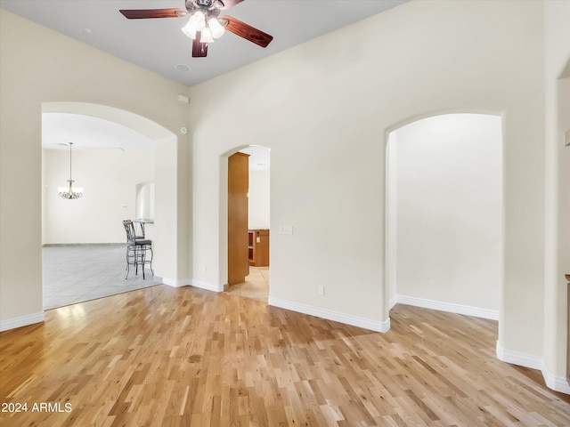 spare room featuring ceiling fan with notable chandelier and light hardwood / wood-style flooring