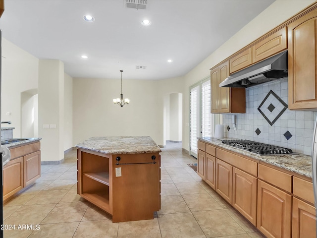 kitchen with stainless steel gas cooktop, light stone counters, tasteful backsplash, decorative light fixtures, and a kitchen island