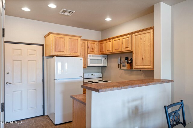 kitchen featuring visible vents, white appliances, a peninsula, and light brown cabinets