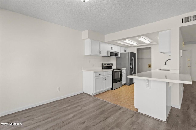 kitchen with light wood-style flooring, white cabinetry, visible vents, appliances with stainless steel finishes, and a breakfast bar area