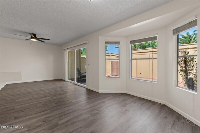 empty room with a wealth of natural light, ceiling fan, wood finished floors, and a textured ceiling