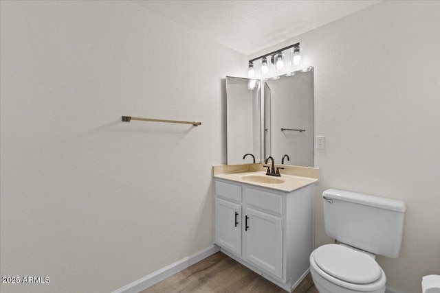 half bathroom featuring toilet, wood finished floors, vanity, and baseboards