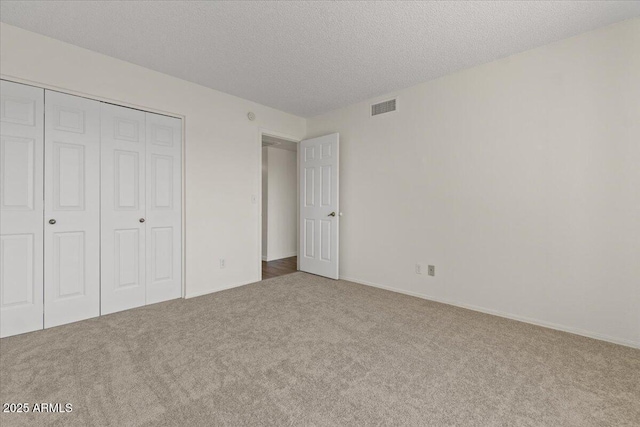 unfurnished bedroom with a textured ceiling, a closet, visible vents, and carpet floors