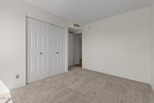 unfurnished bedroom featuring visible vents, a textured ceiling, carpet flooring, and a closet