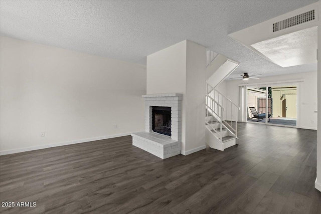 unfurnished living room with a fireplace, stairway, a textured ceiling, visible vents, and dark wood finished floors