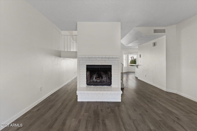 unfurnished living room with visible vents, baseboards, a textured ceiling, a fireplace, and dark wood finished floors