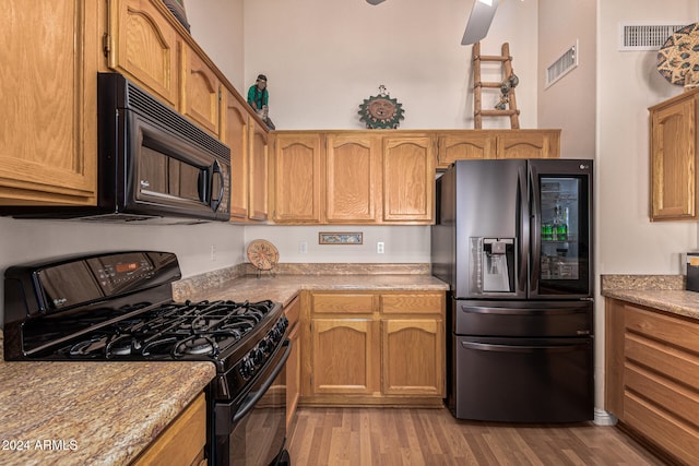 kitchen with black appliances, ceiling fan, light stone counters, and light wood-type flooring