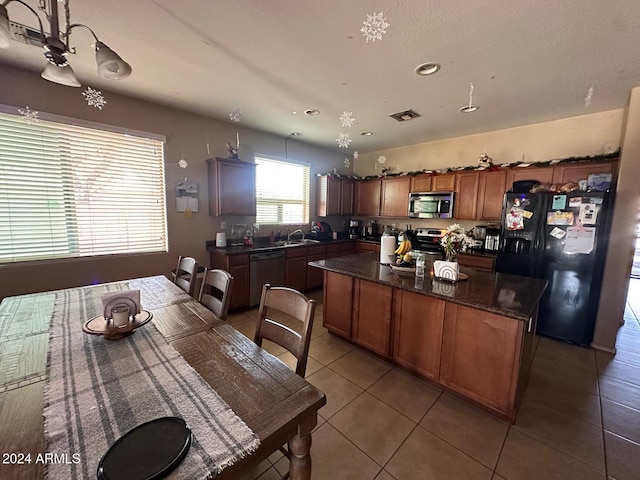 kitchen with sink, a center island, dark stone counters, light tile patterned floors, and appliances with stainless steel finishes