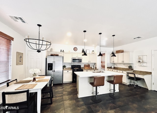 kitchen with white cabinetry, hanging light fixtures, an island with sink, stainless steel appliances, and decorative backsplash