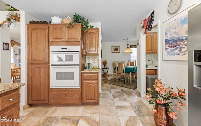 kitchen featuring light stone counters, double oven, decorative light fixtures, and backsplash