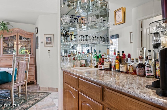 bar featuring sink, light tile patterned floors, light stone counters, and a notable chandelier