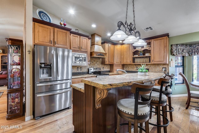 kitchen featuring premium range hood, light stone counters, stainless steel appliances, a breakfast bar, and kitchen peninsula