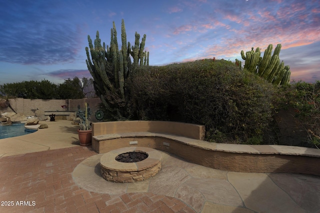 patio terrace at dusk featuring an outdoor fire pit and a fenced in pool