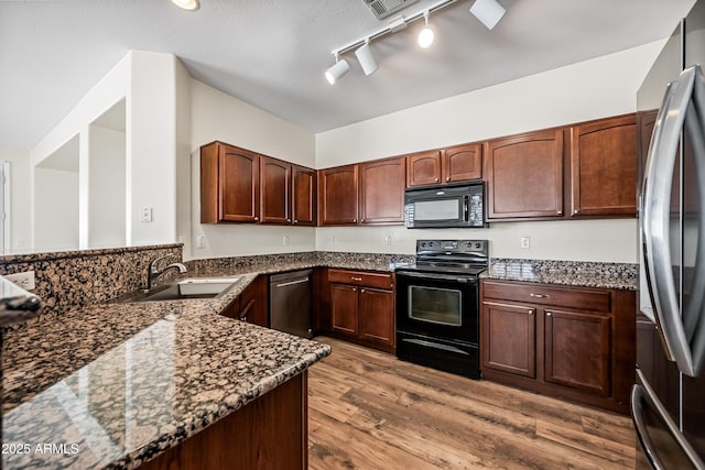 kitchen featuring sink, rail lighting, dark stone counters, wood-type flooring, and black appliances